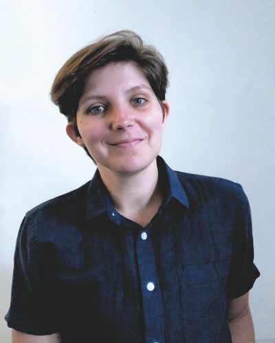 A person with short brown hair and hazel eyes, wearing a navy button down and standing against a white background.