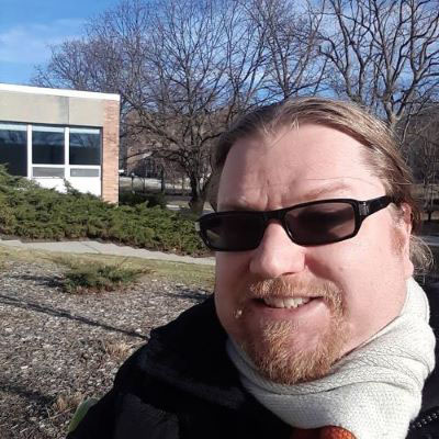 A white man with blond hair and dark glasses sitting outdoors in winter. Photo credit: Dan Smith.