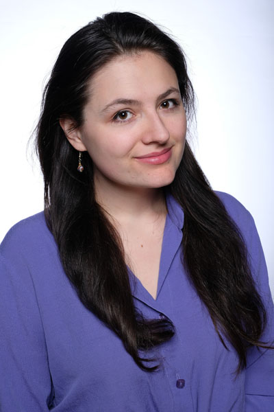A white woman with long brown hair and a purple blouse.