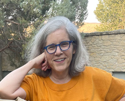 Woman with salt and pepper hair, glasses, and pumpkin-colored blouse. Mark Mezadourian Hughes, photo credit