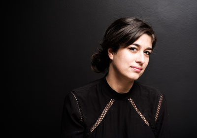 A woman with brown hair, brown eyes and olive skin, wearing a black top. 