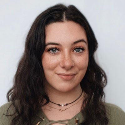 A white woman with blue eyes and brown curly hair in a green shirt against a white background. 