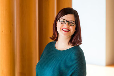 A white woman with brown shoulder length hair wearing glasses.