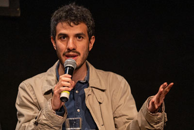 A Mexican man with dark curly hair talking at the mic