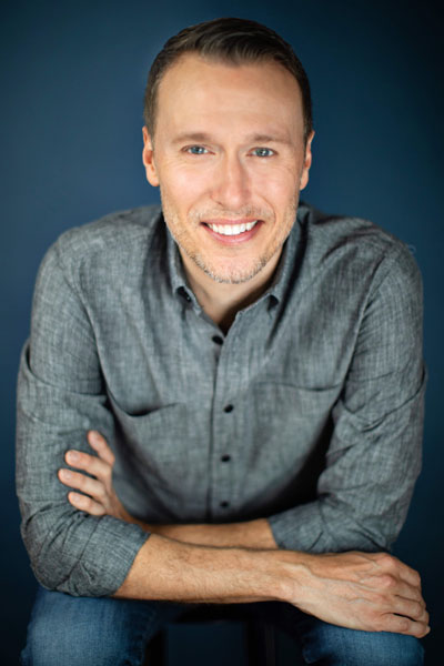 A white person with blonde hair in a grey button down shirt
