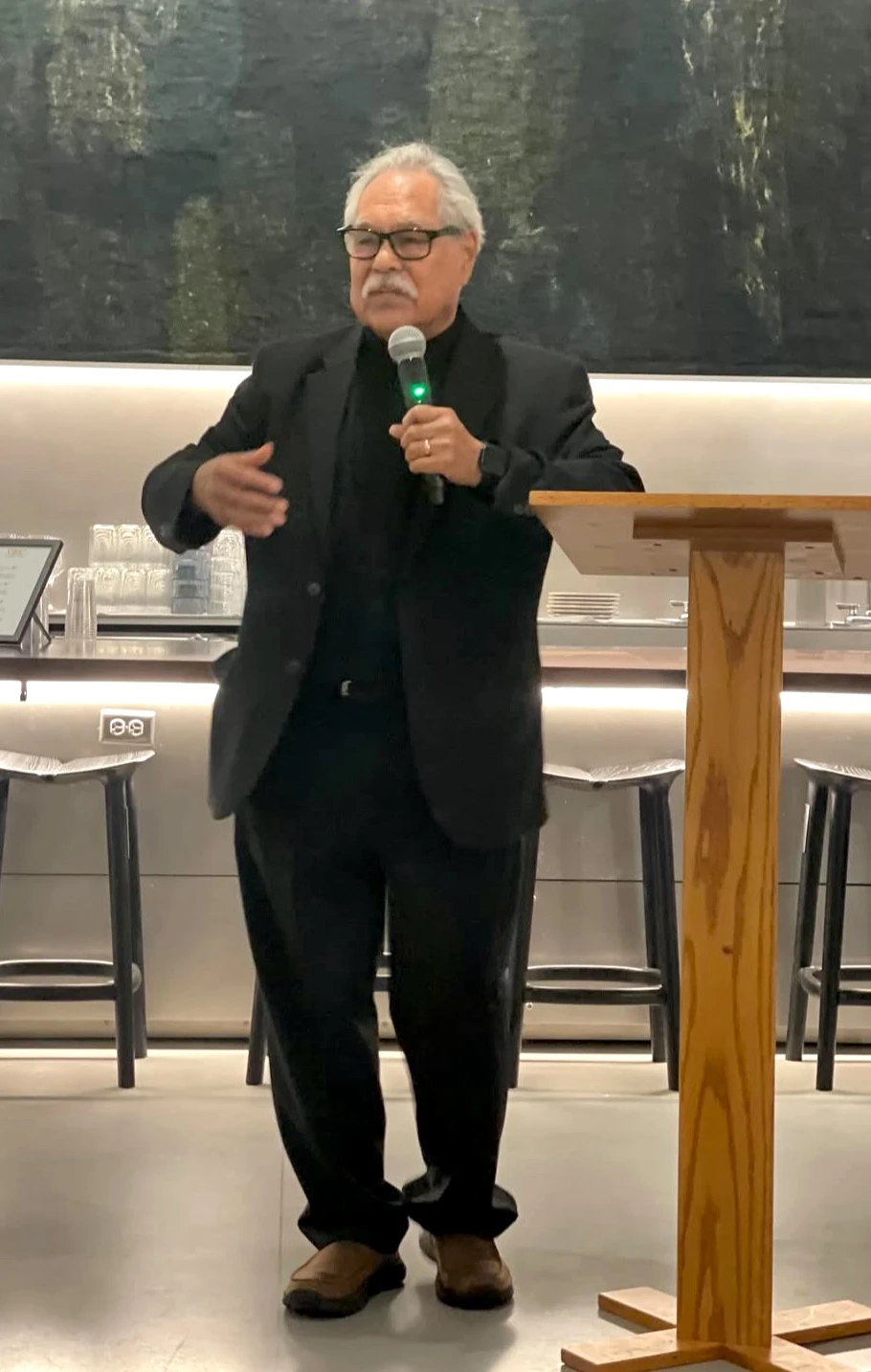 A man in a black suit, Luis Valdez, speaks at the banquet, addressing the attendees with confidence.