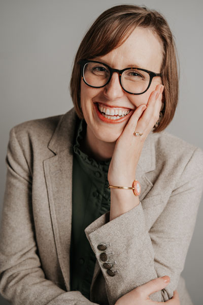 Una mujer blanca con cabello castaño, gafas y una gran sonrisa. Crédito de la foto: Caitlin Strom