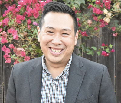 Chinese-American man in a grey blazer with stylish hair and a broad smile.