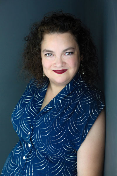 Una mujer sonriente con cabello oscuro y rizado con un vestido azul.