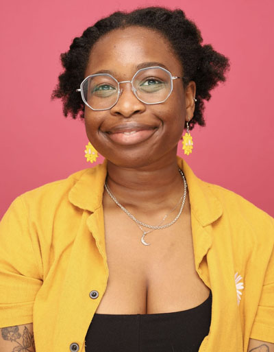 Kemi is a Black femme who wears glasses, her hair is often changing colours and lengths.