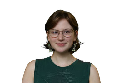 Una persona blanca con gafas de metal, pendientes de mariposa y una camisa verde sin mangas.