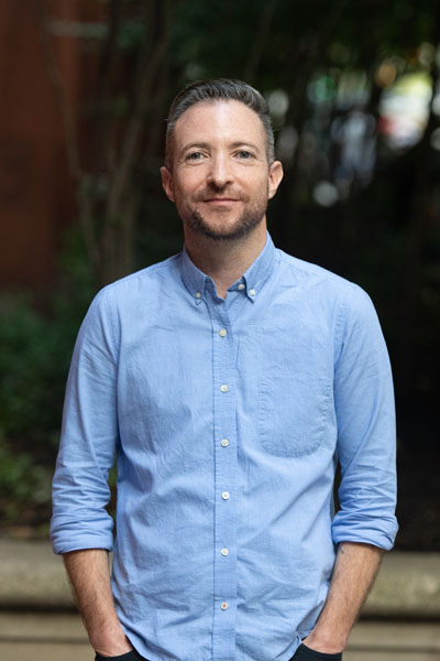 Una persona trans masculina blanca con cabello castaño que viste una camisa azul.